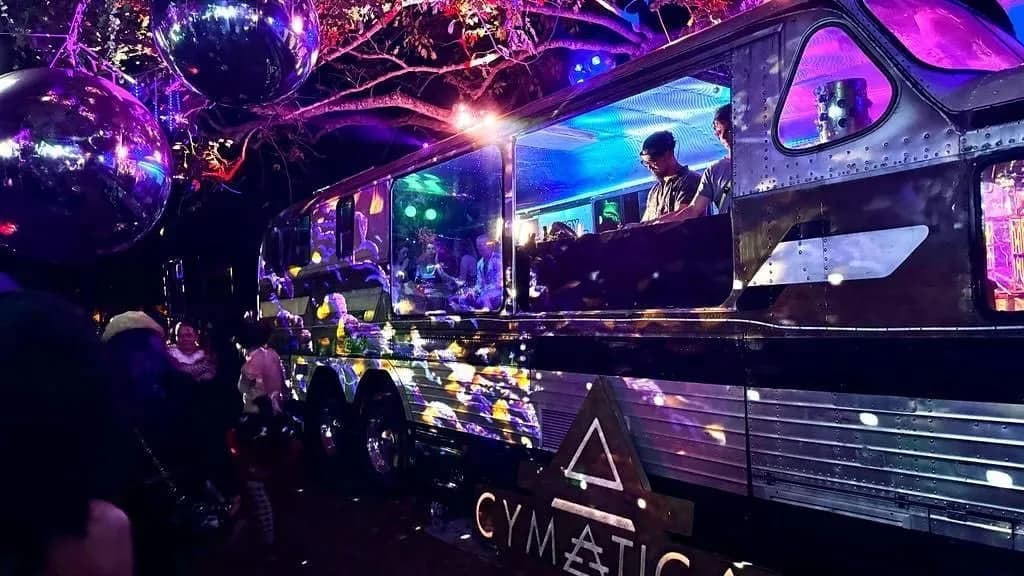 DJs playing from the window of Cymatica's silver bus at night, disco balls strung from the trees above it.